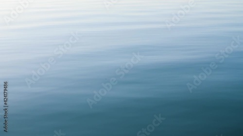 Organic and natural blue water background with soft waves and ripples. Real and clear water surface of a lake or sea with relaxing movements. Copy space. Slow motion, 4K.
