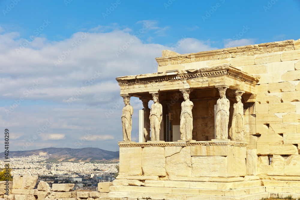 Greece. Acropolis of Athens. Famous gallery with six beautiful statues of caryatids supporting architrave in Erechtheion against backdrop of city of Athens and blue sky. Travel and excursions