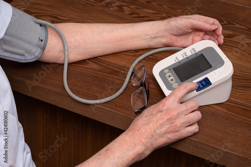 elderly woman suffering from hypertension measures her blood pressure using an electronic monitor. High blood pressure and poor eyesight. Health of the elderly