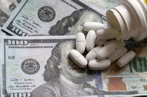 White phyto pills poured from a bottle on a background of US dollar bills. with copy space, shallow depth of field. The concept of medicine, expensive drugs. photo