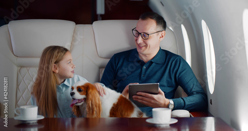 Fotografie Mature businessman travelling on personal jet with little daughter and dog