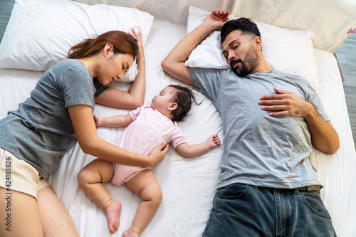 Family relax bedtime togetherness lifestyle concept. Parenthood with their little mixed race daughter sleeping calm together on the white bed at home.