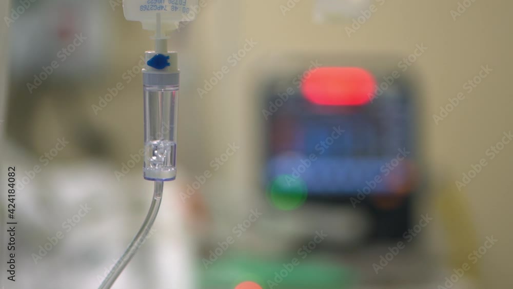 An intravenous drips fluid and medication into a patient with COVID-19 while a monitor sounds a warning alarm - focus pull
