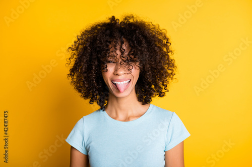 Photo of sweet childish dark skin wavy lady wear blue t-shirt showing tongue out isolated yellow color background