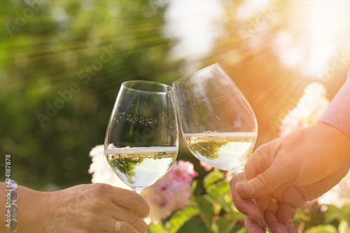 Couple romantically celebrate outdoors with glasses of white wine, proclaim toast People having dinner in a home garden in summer sunlight.