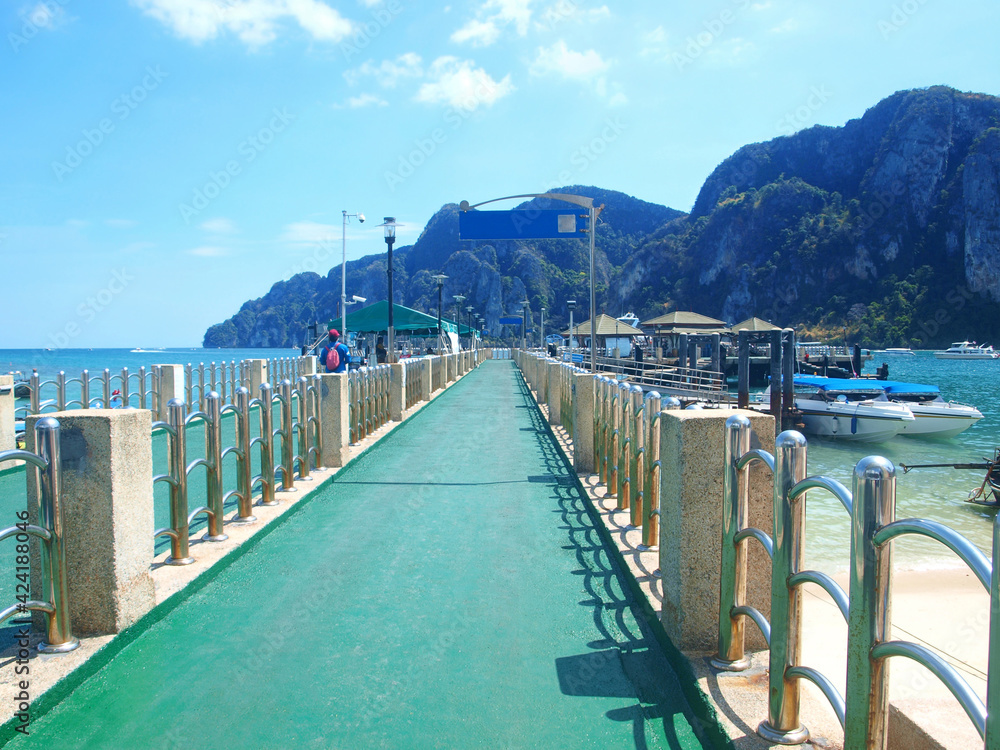 Pier in Ko Phi Phi Thailand. Island Phuket water area. Sea trip, cruise, tour tourism. People on the pier, boats, longtail boats. Rocky cliff covered with green forest on background. Beautiful bridge