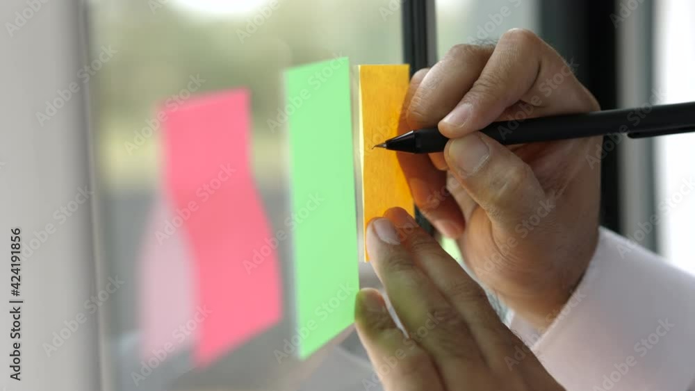 Business male writing note on the Colorful of post it on the wall. sticky note or paper note on the windows for note what to do in the office.