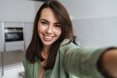 Young happy woman smiling while taking selfie photo at home kitchen