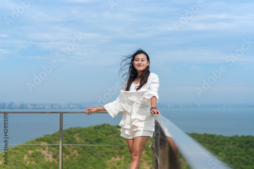 windy hair Asian woman standing and looking forward with happiness at terrace view point on mountain peak island, Koh Larn high view point, Chonburi, Thailand © Thitiporn