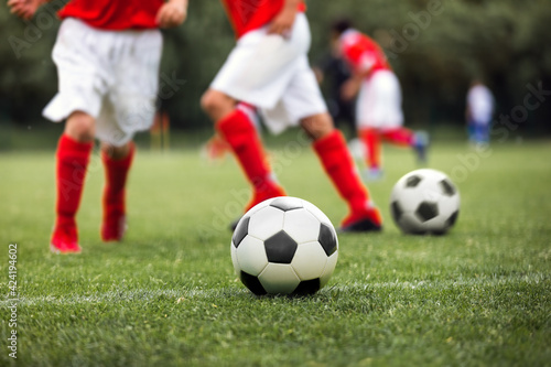 Closeup of soccer ball on grass pitch. Kid kicking classic black and white football balls on training. School children on soccer playfield. Kids practicing sports on grass field
