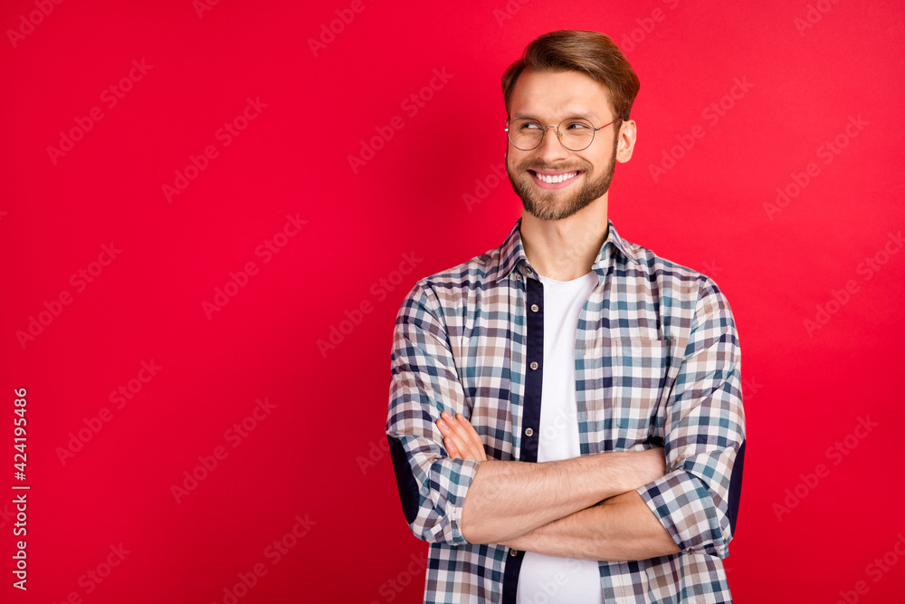 Photo of charming handsome young guy wear checkered shirt glasses arms crossed looking empty space isolated red color background Photo of charming handsome young guy wear checkered shirt glasses arms crossed looking empty space isolated red color background