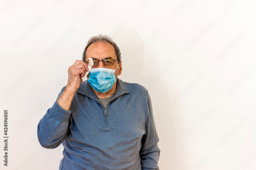 Portrait of a senior man with misted glasses due to protective face mask. Foggy glasses by wearing face mask. Mature man is cleaning his eyeglasses by getting wet because of wearing face mask. Portrait of a senior man with misted glasses due to protective face mask. Foggy glasses by wearing face mask. Mature man is cleaning his eyeglasses by getting wet because of wearing face mask.