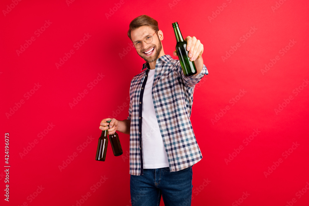 Photo of pretty sweet young gentleman dressed plaid shirt spectacles smiling holding beer bottles isolated red color background Photo of pretty sweet young gentleman dressed plaid shirt spectacles smiling holding beer bottles isolated red color background