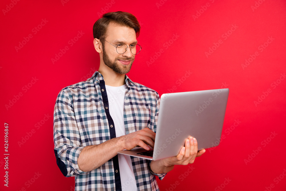 Photo of handsome confident young guy wear checkered shirt typing modern gadget smiling isolated red color background Photo of handsome confident young guy wear checkered shirt typing modern gadget smiling isolated red color background