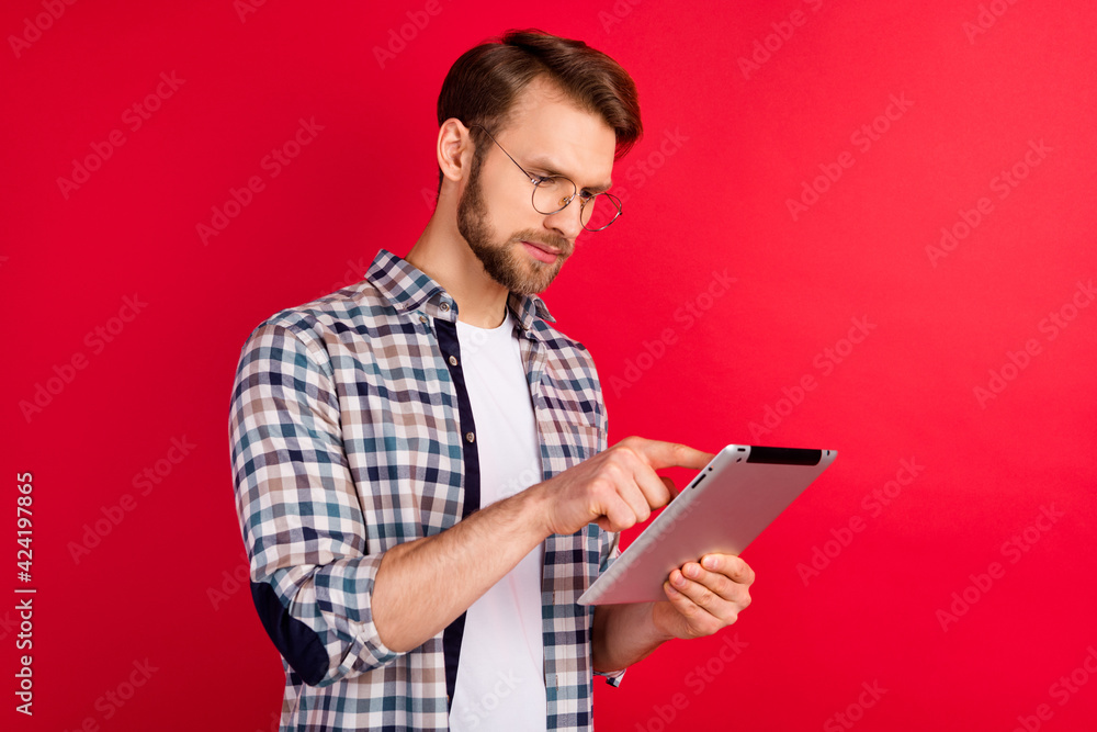 Photo of busy pretty young gentleman dressed plaid shirt spectacles browsing modern gadget isolated red color background Photo of busy pretty young gentleman dressed plaid shirt spectacles browsing modern gadget isolated red color background