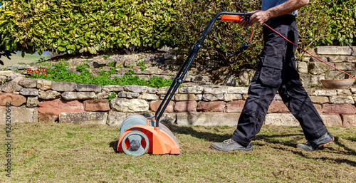 Using a scarifier in the garden to improving quality of the lawn in spring. male worker man, Gardener Operating Soil Aeration Machine on Grass Lawn. Aeration with a scarifier. Lawn thatcher in action.