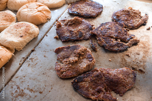 Overcooked and burned burger patties on a large flat gas griddle at a burger joint photo