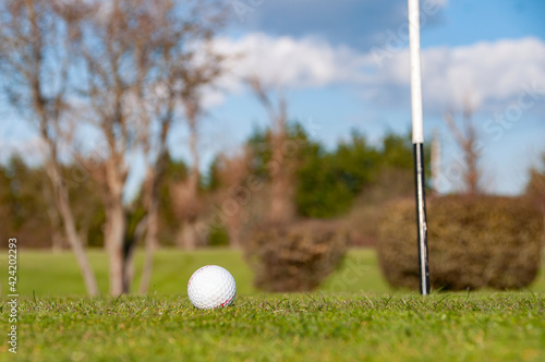 Closeup of a Golf ball beside flag pole.