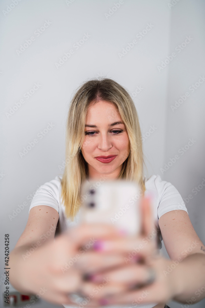 Chica rubia risueña usando smartphone y sonriendo sobre fondo blanco