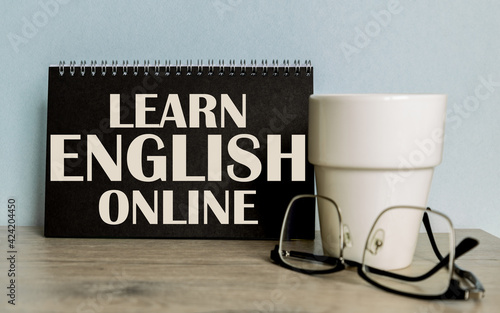 Text LEARN ENGLISH ONLINE . mug, glasses, black notebook for information on the wooden table