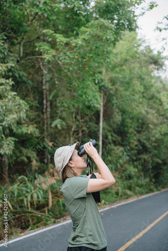 Back view of young asian woman with hiking hat looks through binoculars between a travel.