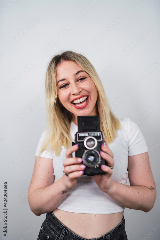 Young Caucasian female from Spain taking a selfie with a camera against a white wall
