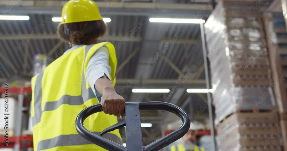 Back view of african female warehouse worker using hand pallet truck Back view of african female warehouse worker using hand pallet truck