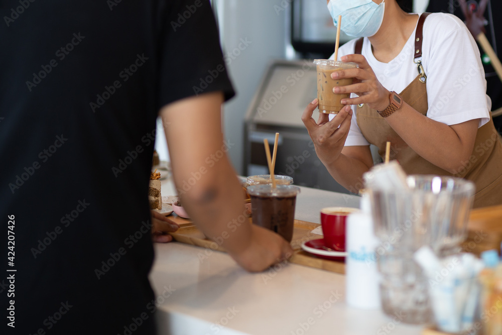 Waitress wearing protection face mask serving iced coffee drink to customer in cafe.