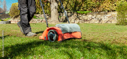 Using a scarifier in the garden to improving quality of the lawn in spring. male worker man, Gardener Operating Soil Aeration Machine on Grass Lawn. Aeration with a scarifier. Lawn thatcher in action.