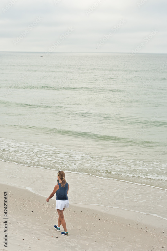 top view, very far away, walking a sandy, tropical beach, shoreline, while talking on a cellphone, with overcast day