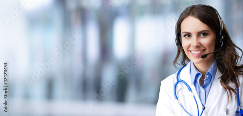 Portrait of happy smiling female doctor in headset, over blurred modern office background, copy space area for slogan or text. Medical call center concept picture. photo