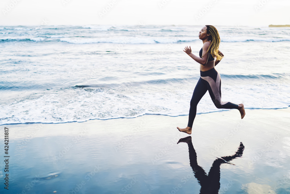 Black young female in active clothes reaching running goals on cardio workout in morning, slim dark skinned energetic sportive woman training athletic strength outdoors jogging around seashore Black young female in active clothes reaching running goals on cardio workout in morning, slim dark skinned energetic sportive woman training athletic strength outdoors jogging around seashore