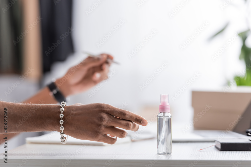 Cropped view of african american businessman pulling hand to sanitizer in showroom