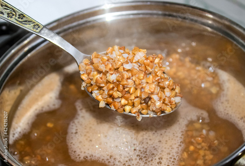 Photos Buckwheat in a spoon on the background of a pan with buckwheat groats