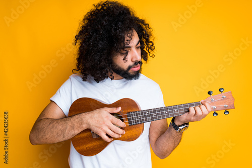 Young african american musician holds a ukulele in his hands and plays on it by playing the strings