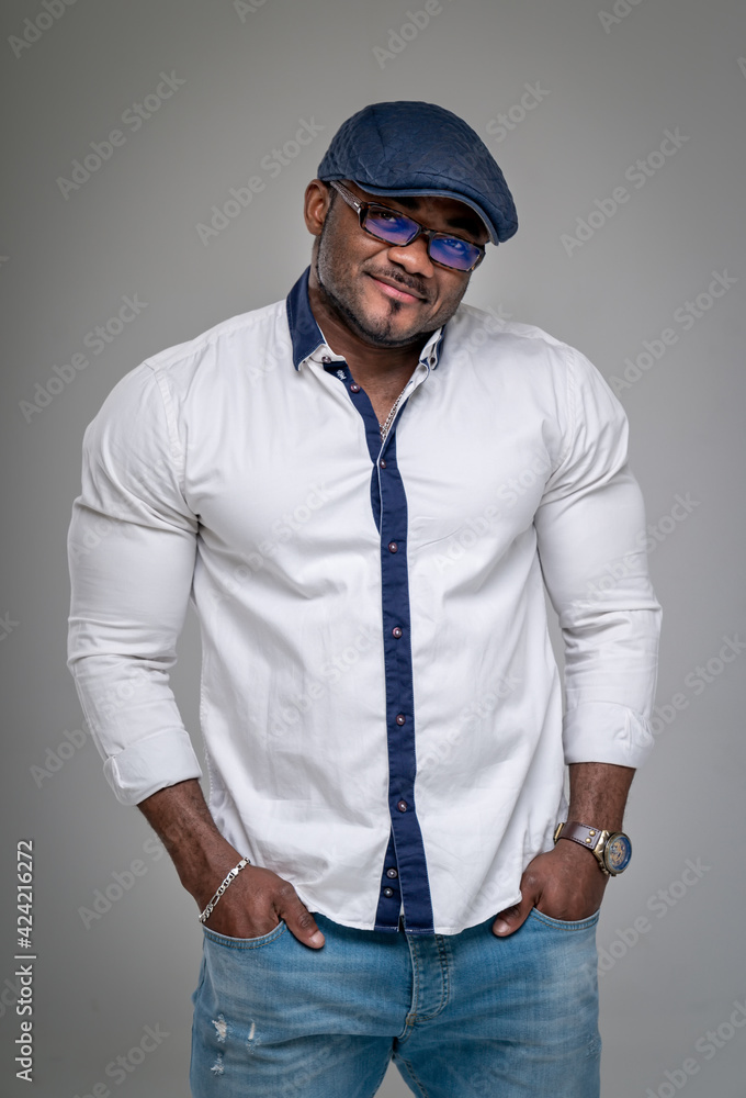 African American millennial male in glasses and cap isolated on grey studio background. Black man keeps hands in pockets. Closeup. African American millennial male in glasses and cap isolated on grey studio background. Black man keeps hands in pockets. Closeup.