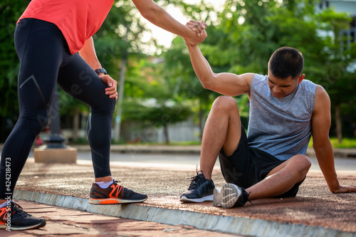 Fototapeta Naklejka Na Ścianę i Meble -  Asian male runner sustained a knee injury while exercising and was helped by a fitness partner. Concept of health care and sports
