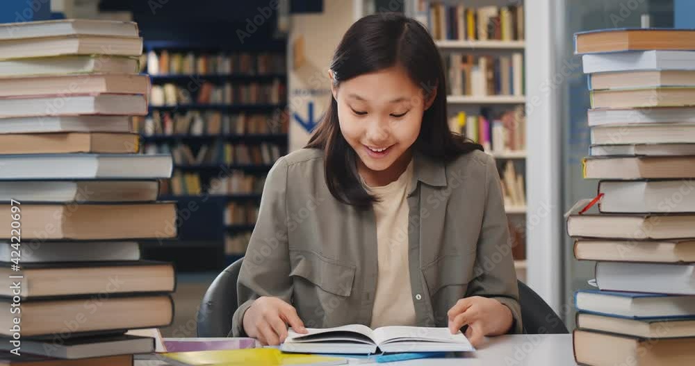 Asian school student girl reading book sitting at desk at library Asian school student girl reading book sitting at desk at library