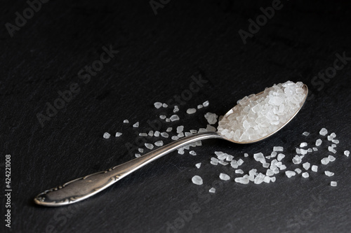 gross white sea salt on a silver spoon black background