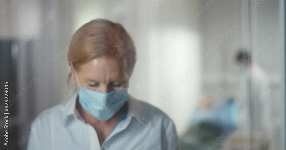 Female mature doctor taking off face mask in hospital standing near window Female mature doctor taking off face mask in hospital standing near window
