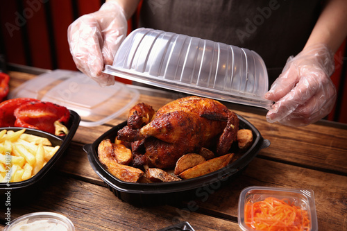 Canvas-taulu Waiter in gloves closing container with fresh prepared meal at wooden table, closeup