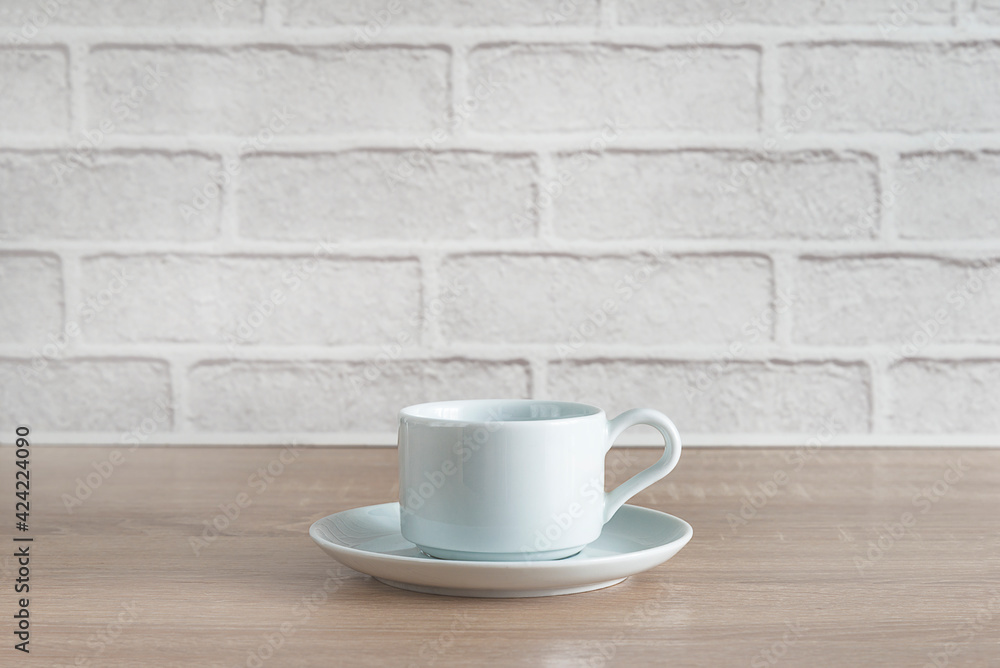 White cup of coffee on wooden table in front of white brick wall White cup of coffee on wooden table in front of white brick wall