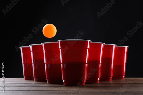 Canvastavla Plastic cups and ball for beer pong on wooden table against black background