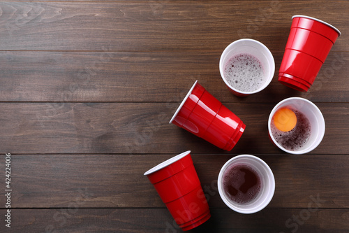 Plastic cups and ball on wooden table, flat lay with space for text. Beer pong game