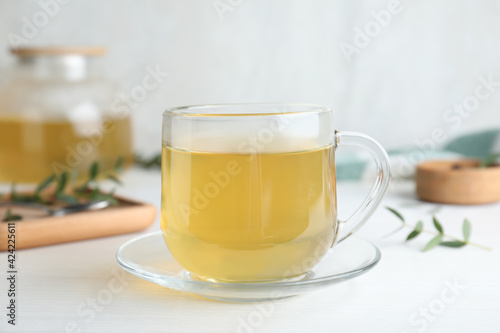 Glass cup of aromatic eucalyptus tea on white wooden table, closeup