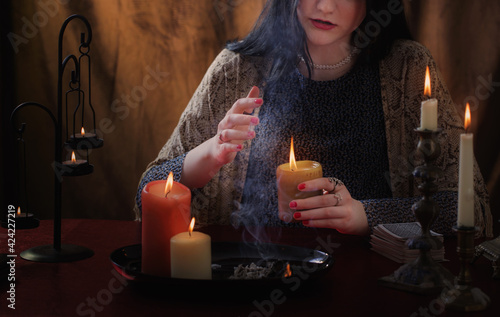 young witch conjures with burning candles on  dark background