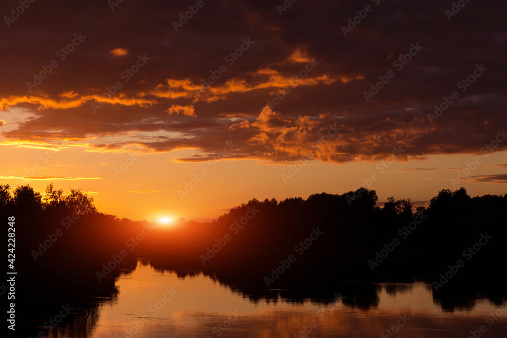 Sunset, sunrise on storm sky with dark clouds, orange yellow red sun and sunlight in reflection of river, lake water Sunset, sunrise on storm sky with dark clouds, orange yellow red sun and sunlight in reflection of river, lake water