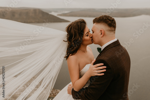 loving couple wedding newlyweds outdoor. bride in white dress long veil and groom in suit walk in summer fall on mountain above river. sunrise. man and woman on rocks above cliff. bakota ukraine photo