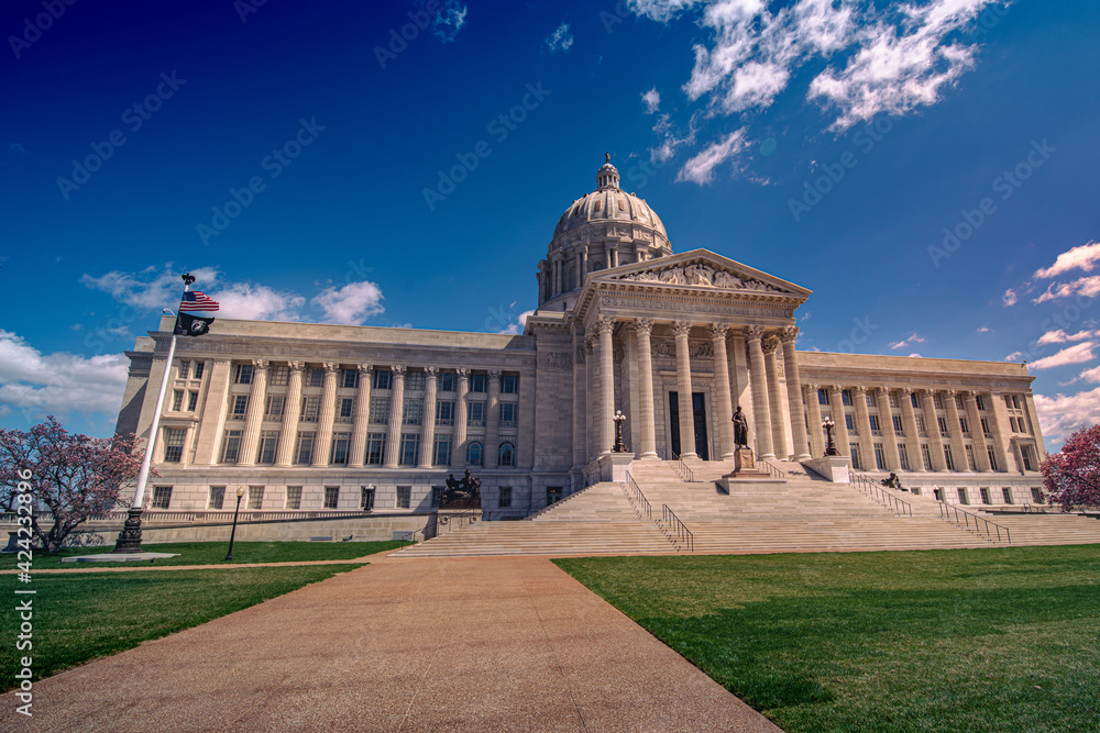 Low angle view of sidewalk leading up to the marble domed and columned Missouri state capitol building in Jefferson City in spring with blue sky.