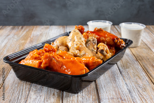 Photography A view of a to-go container of assorted flavors of chicken wings.